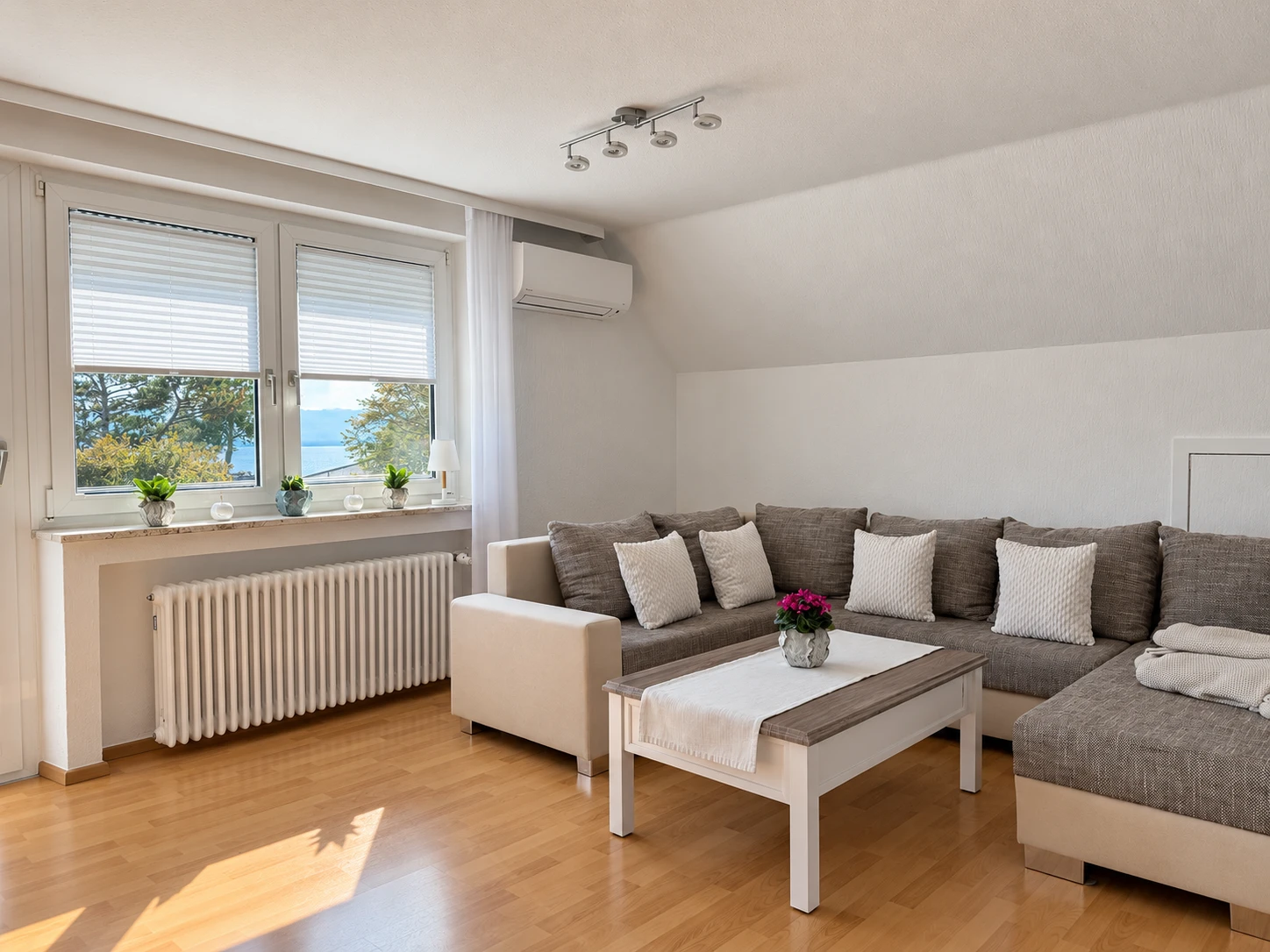 Wohnzimmer der Ferienwohnung mit Ecksofa, Klimaanlage und Blick zum See